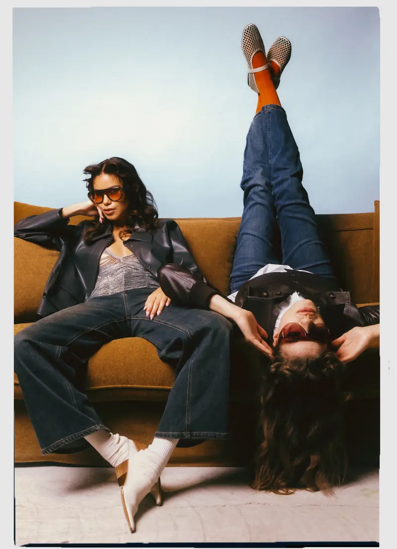 Look L10, Fall Winter 26/27: due modelle sul divano in giacca nera e jeans, una a testa in giù