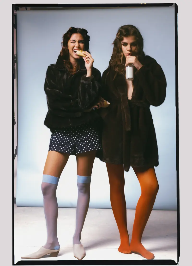 Look L3,5, Fall Winter 26/27: due modelle in piedi con giubbotti di pelliccia scura, calze azzurre e arancio